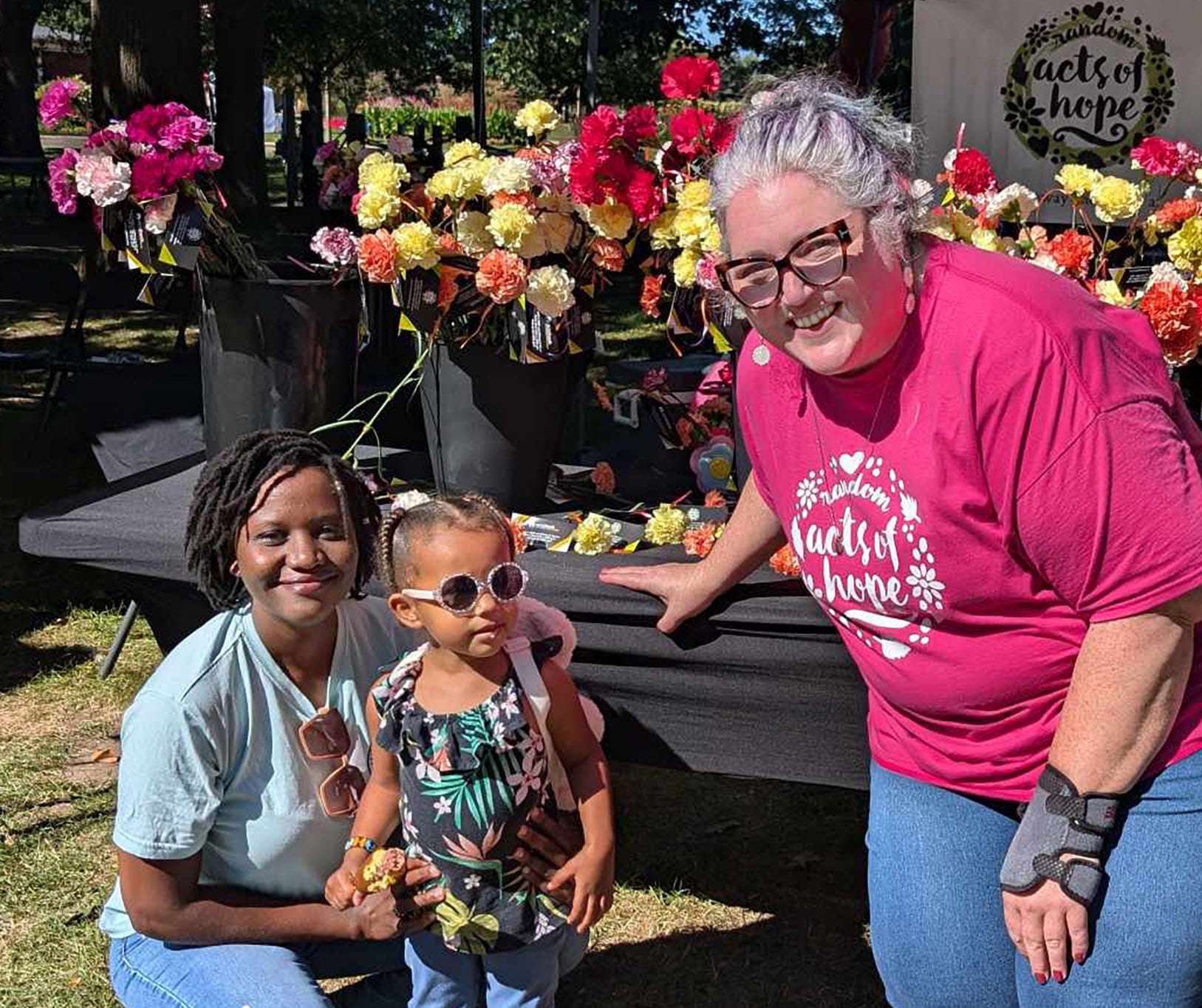 Two women and a child smile for a photo in front of a table adorned with vibrant flowers.