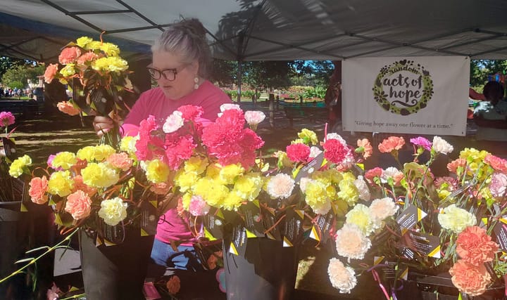 A woman stands before a table decorated with an array of flowers.