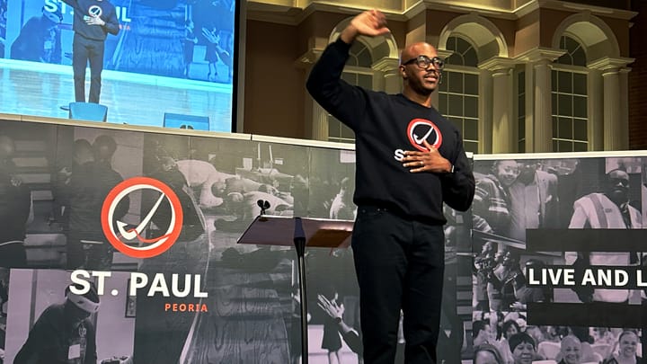 MIddle-aged man preaches from a stage with a screen and mural behind him.